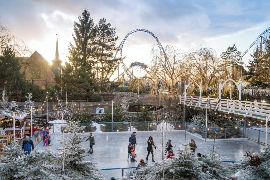 Eine Eislaufbahn im Freien, umgeben von Bäumen, mit einer Achterbahn im Hintergrund.