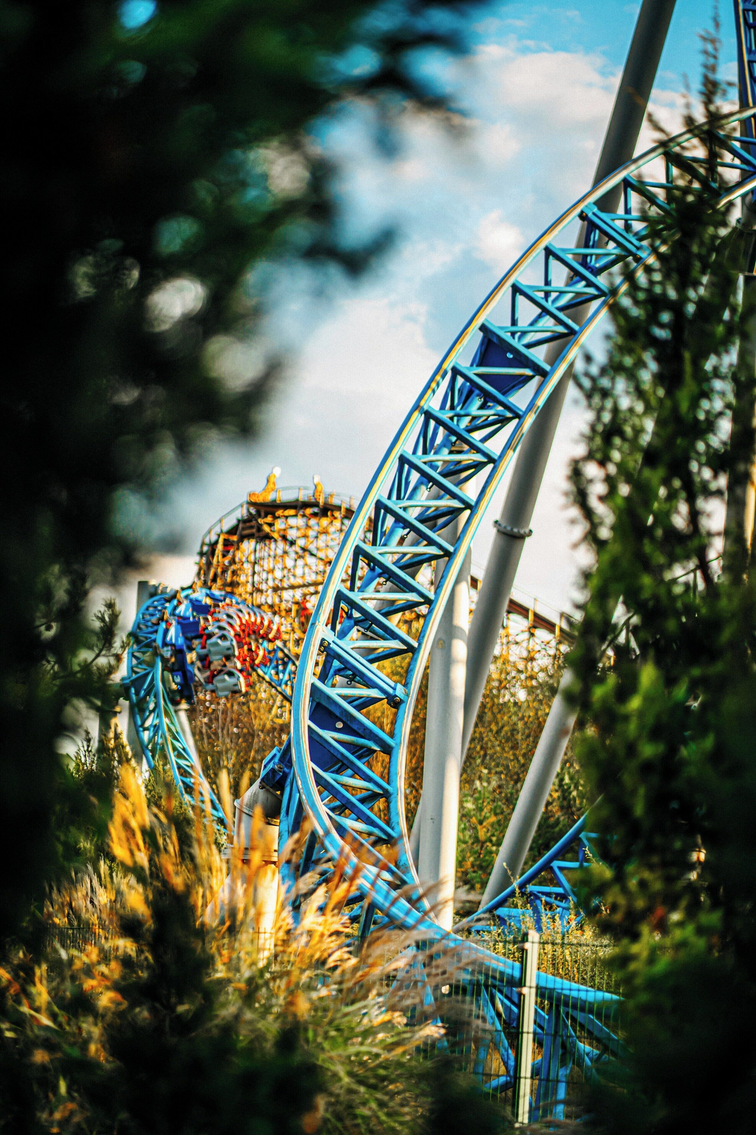 A roller coaster with a blue track, surrounded by trees and a cloudy sky.