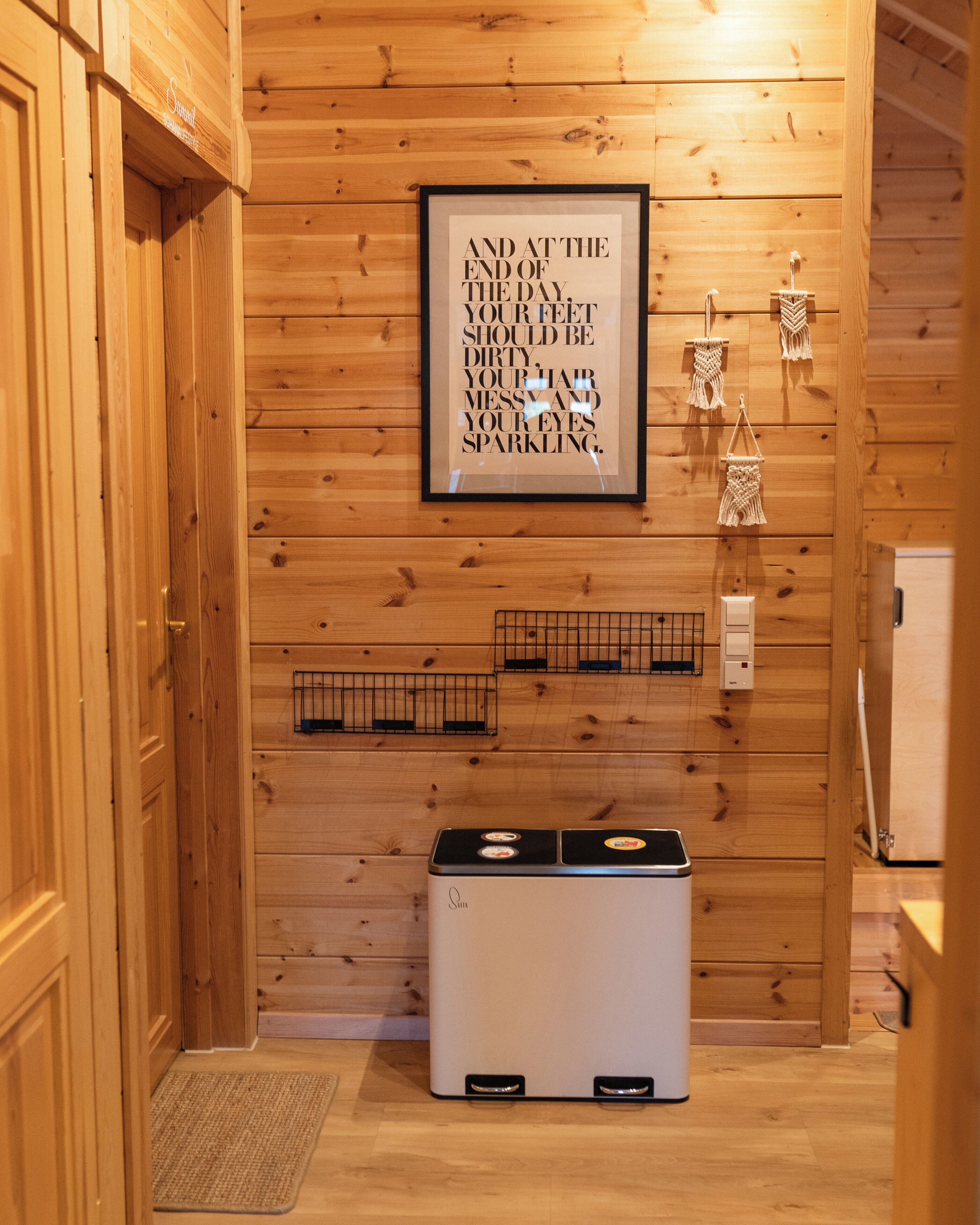 A wooden-paneled room with a framed motivational quote, a small heater, and a macrame wall hanging.