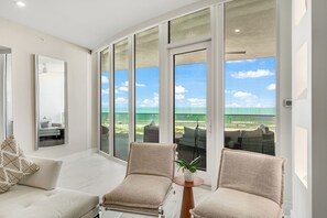 Ein modernes Wohnzimmer mit einem großen Glasfenster, das auf einen Balkon mit Blick zum Strand führt.
