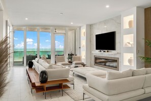 A modern living room with a large TV, comfortable seating, and a view of the ocean. - Luxury Oceanfront Condo in Cocoa Beach (Cocoa Beach)
