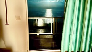 Habitación con vista a un cuerpo de agua a través de una ventana, piso de madera y cortina verde.