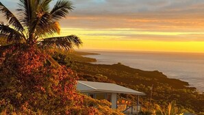 Una propiedad costera con vista al océano al atardecer, rodeada de vegetación exuberante y un pequeño edificio con balcón.