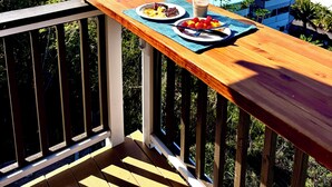 Una terraza de madera con una mesa dispuesta para una comida, con vista a un paisaje costero con edificios y palmeras.