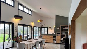 A spacious dining area with a round table and chairs, a kitchen with wooden cabinets, and large windows offering a view of the outdoors. - Modern haven of peace with panoramic views (Saint-Caprais-de-Bordeaux)
