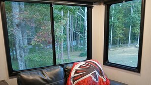 A black leather sofa with a red and black pillow in a room with two windows overlooking a wooded area. - 2-bedroom recreational vehicle in enchanting Cartersville with AC (Cartersville)