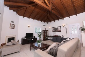 A spacious living room with a high wooden ceiling, a fireplace, a television, and a dining area with a table and chairs. - Villa Sophia (Corfu)