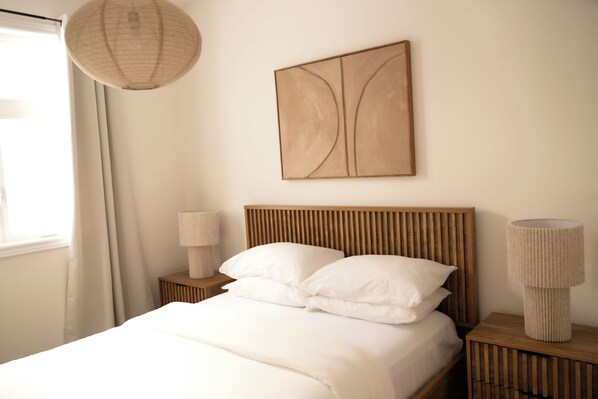 A neatly made bed with white linens, a wooden headboard, and a wall-mounted abstract painting.
