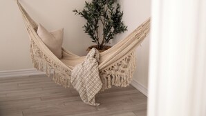En hængekøje med en beige pude og et mønstret tæppe, en potteplante og trægulv.
