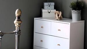 A corner of a room with a white dresser, a framed picture on the wall, and a plant in a white pot. - Beds at 46 (Cowes)