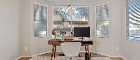 A corner office with a desk, chair, and large windows with blinds.