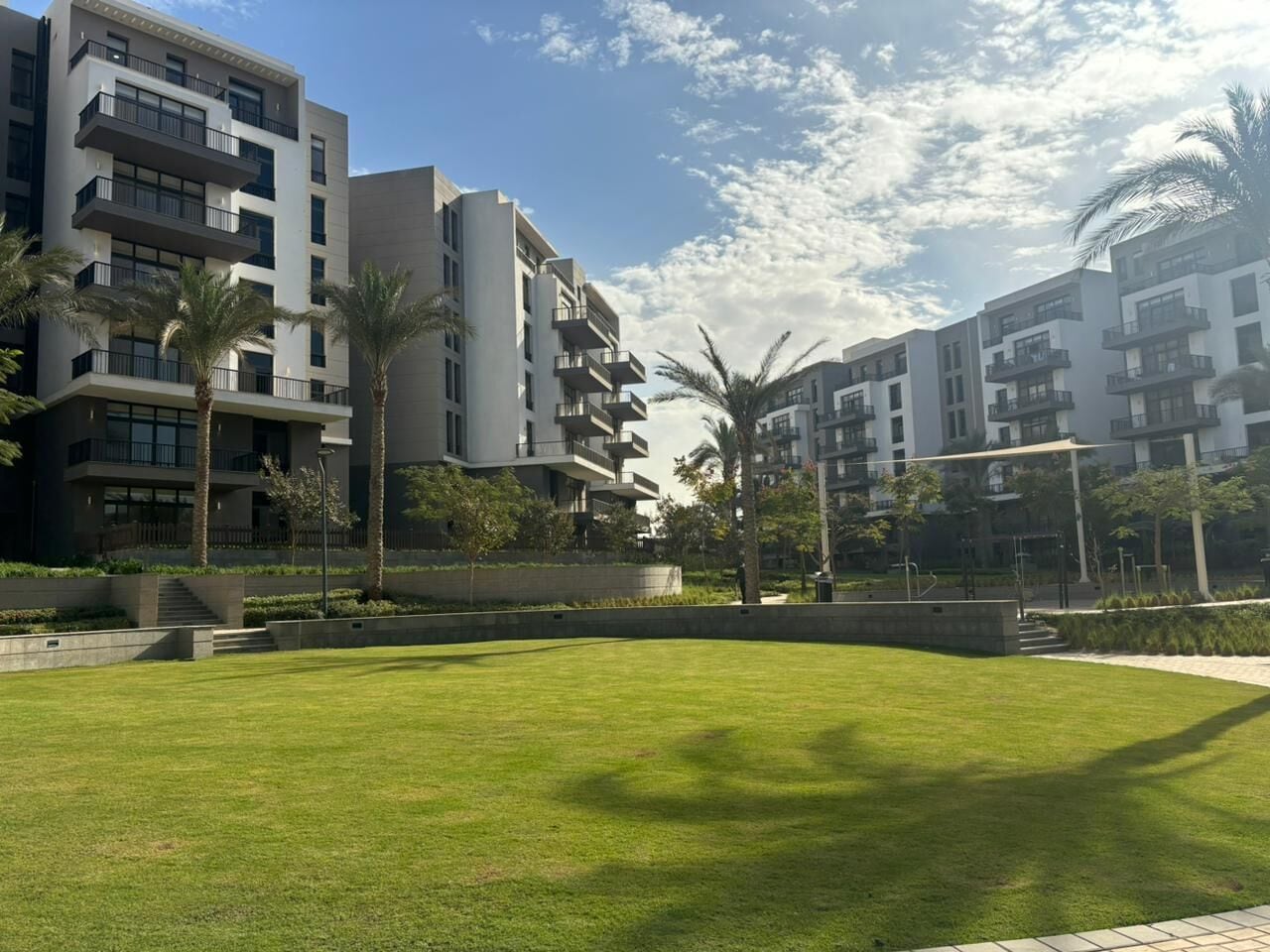 A modern apartment complex with multiple balconies, a well-maintained lawn, and palm trees.