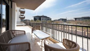 A balcony with wicker furniture, a glass table, and a view of surrounding buildings. - Elegant 2BR Serviced Apart at Cairo Festival City (Cairo Governorate)