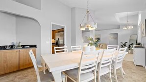 A modern dining area with a wooden table and white chairs, a kitchen in the background, and pendant lighting. - Stylish Private Heated Pool, close to beach (Port Charlotte)