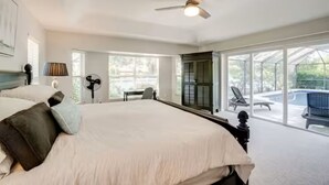 A spacious bedroom with a large bed, a ceiling fan, and a view of the outdoor patio. - Stylish Private Heated Pool, close to beach (Port Charlotte)