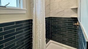 Un baño con ducha, ventana y una combinación de azulejos blancos y azul oscuro.