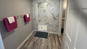 Een badkamer met marmeren wanden, een houten vloer en twee handdoeken aan een rek.