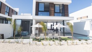 Et moderne hus med to etager, en pool, udendørs møbler og en overdækket terrasse.