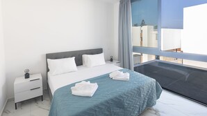 Et moderne hotelværelse med en stor seng, et natbord og udsigt over byen gennem et stort vindue.