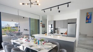A modern kitchen with a central island, stainless steel appliances, and a dining area with grey chairs and a white table set for six. - Protaras Aqua Pearl Villa AQ12 by Interhome (Protaras)