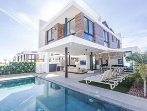 Une maison moderne à deux étages, dotée d’une piscine, d’un espace salon extérieur et d’un grand écran de télévision.