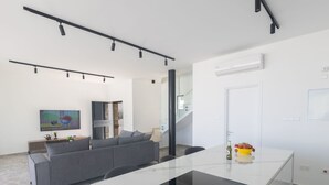 A modern kitchen with a central island, a grey sofa, and a dining table. - Protaras Aqua Pearl Villa AQ05 by Interhome (Protaras)