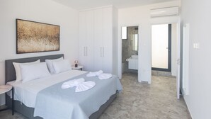 A modern bedroom with a large bed, a bedside table, a wardrobe, and a bathroom visible through an open door. - Protaras Aqua Pearl Villa AQ05 by Interhome (Protaras)