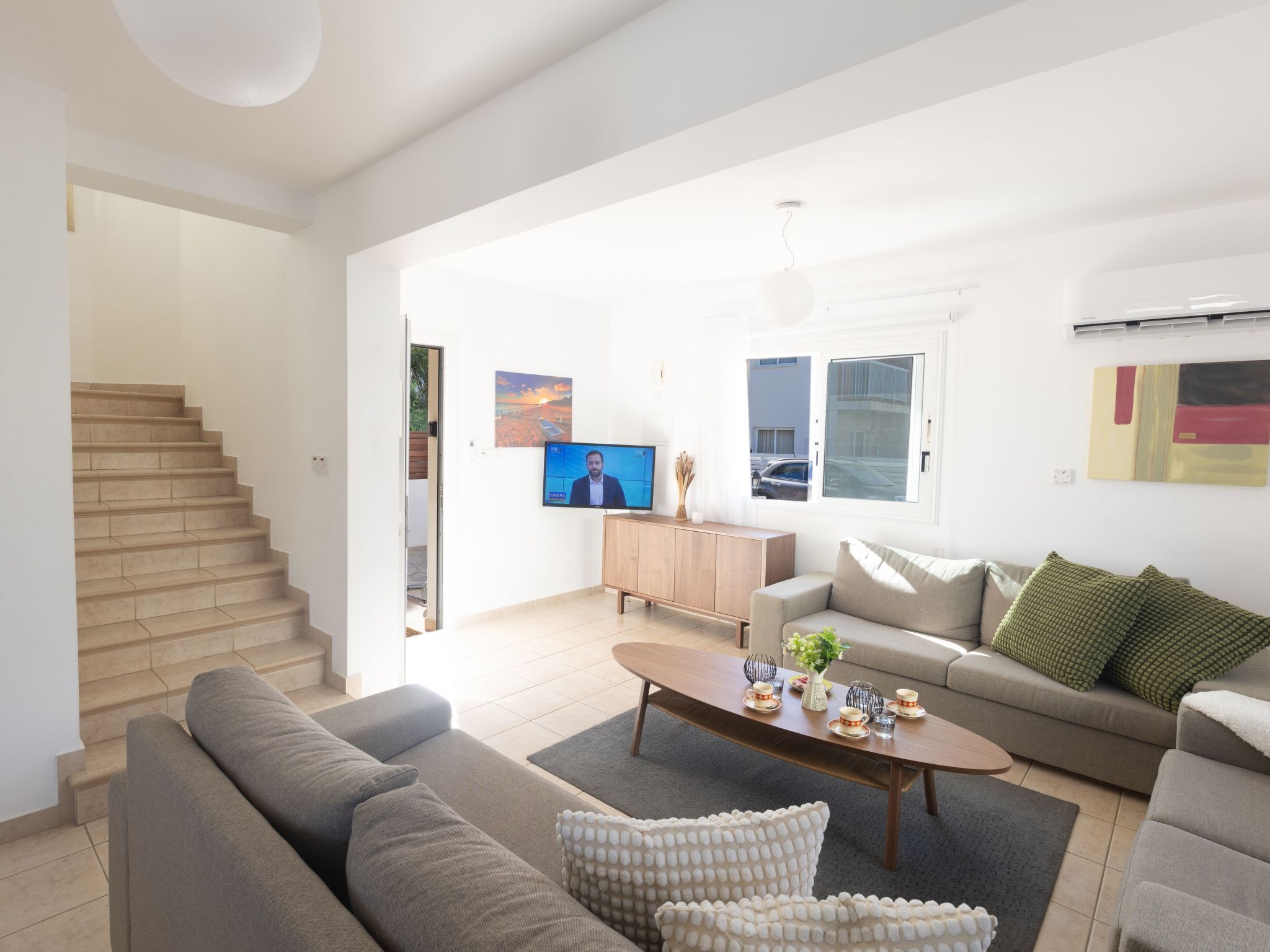 Ein modernes Wohnzimmer mit Sofa, Couchtisch und Fernseher. Eine Treppe ist links zu sehen.