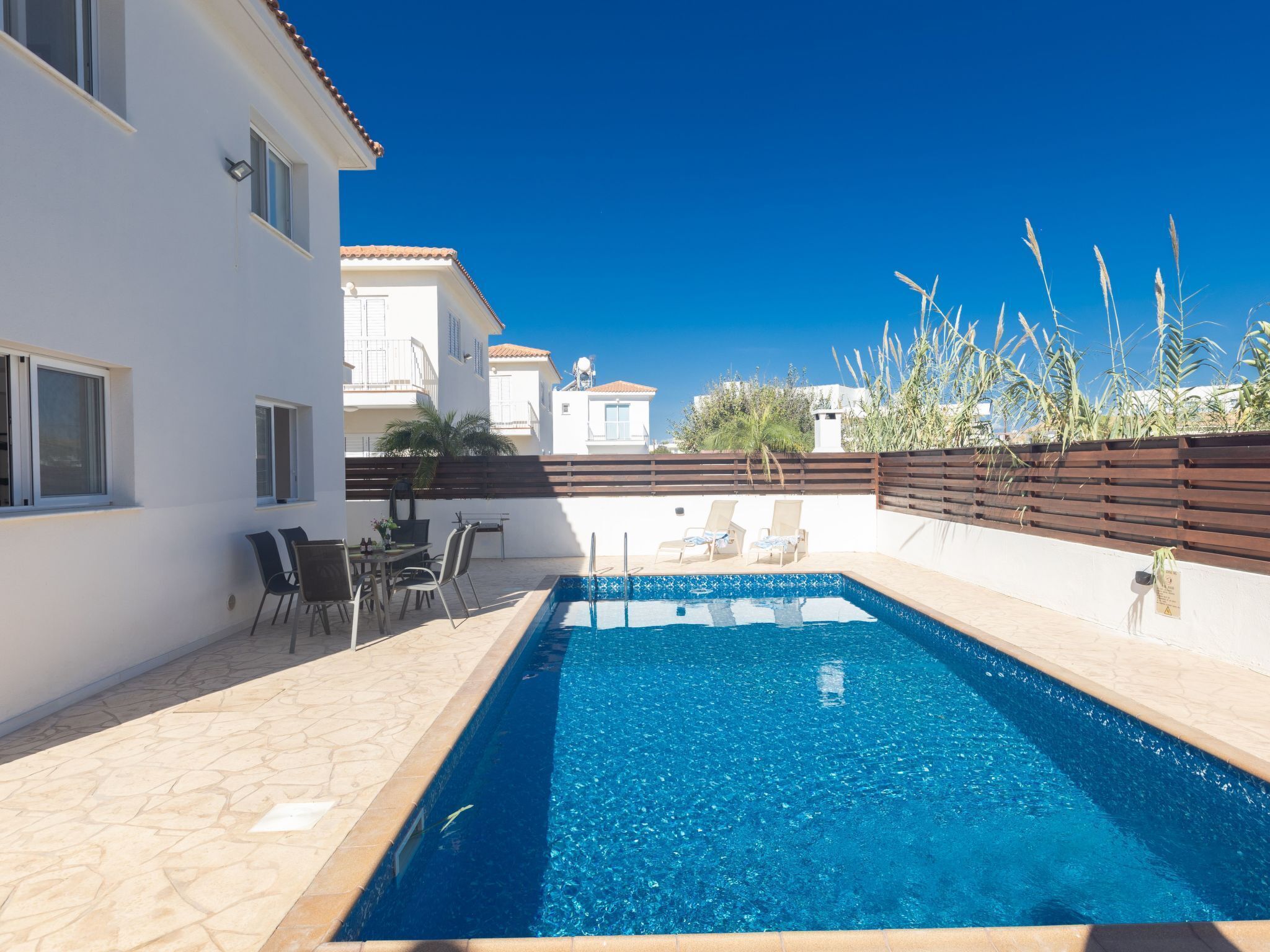 Una piscina amb terrassa enrajolada, gandules i una zona de menjador amb taules i cadires.