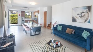 A modern living room with a blue sofa, a glass dining table, and a kitchen in the background. - Ayia Napa Satin Villa SVI3 by Interhome (Ayia Napa)