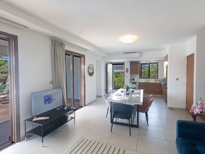 Ein modernes Wohnzimmer mit Fernseher, eine Essecke mit Tisch für vier Personen und eine durch eine offene Tür sichtbare Küche.