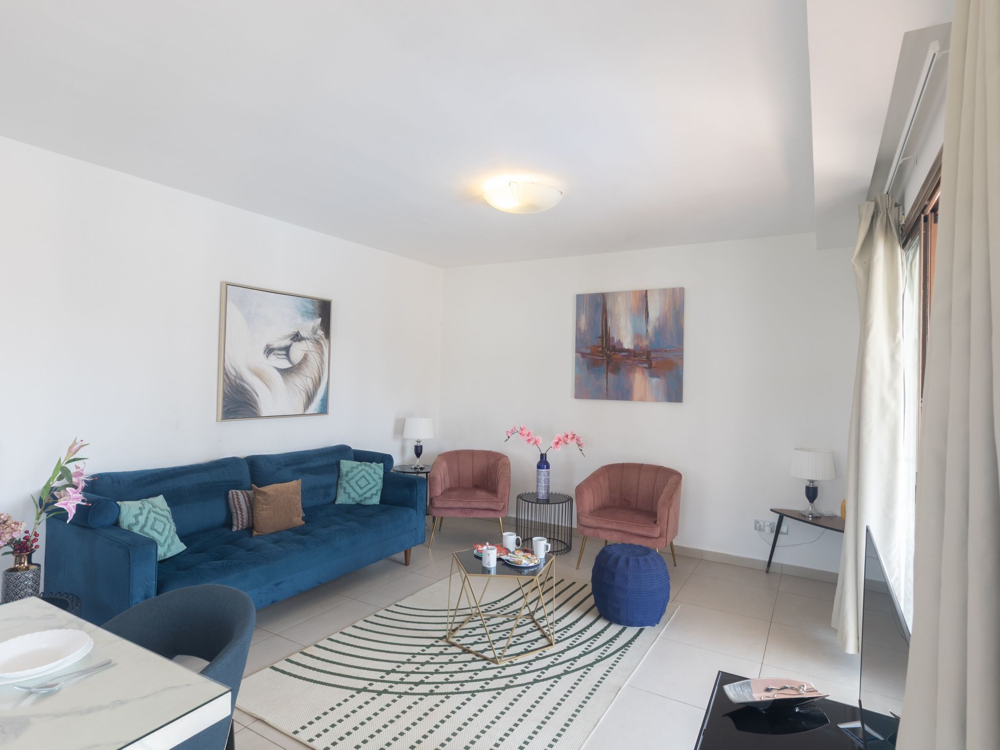 A modern living room with a blue sofa, two armchairs, a coffee table, and artwork on the walls.