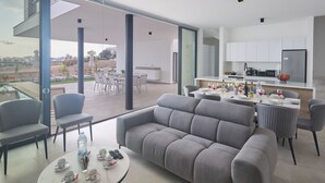 Een moderne woonkamer met een grijze bank, een eettafel voor vier personen en een keuken met witte kasten en een zwarte koelkast.