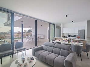 A modern living room with a grey sofa, a dining table set for four, and a kitchen area with white cabinets and a black refrigerator. - Protaras Aqua Pearl Villa AQ11 im Zentrum by Interhome (Protaras)