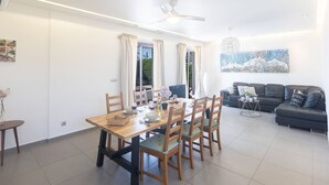 A dining area with a wooden table and chairs, a ceiling fan, and a dining table set with wine glasses and a bowl. - Ayia Napa Satin Villa SVI1 by Interhome (Ayia Napa)