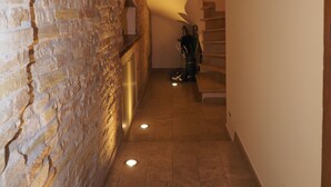Ein schmaler Gang mit Steinwänden, Holzboden und einer Treppe, die nach oben führt.