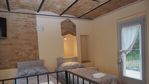 Ein Zimmer mit zwei Betten, einer Ziegelwand, einer Steindecke und einem Fenster mit Vorhang.