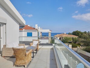 Een balkon met rieten meubels, een glazen hekwerk en uitzicht op zee.