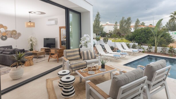 Una sala de estar moderna con un ventanal grande, una piscina y mobiliario exterior.