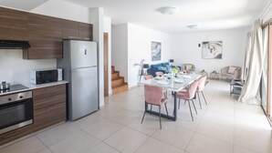 Een moderne keuken met een koelkast, magnetron en fornuis, die uitkomt op een eethoek met een tafel voor vier personen.