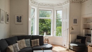 A modern living room with a dark grey sofa, a white coffee table, and a large bay window with a view of greenery. - Viktorianische Villa mit Strandblick by Interhome (Dundee)