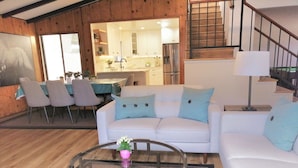 A modern living room with a white sofa, a glass coffee table, and a dining area with a table and chairs. - Bright beach-city home — newly renovated. Only 3 mi. from SoCal beaches!   (Torrance)