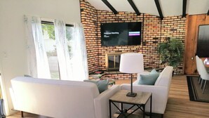 A living room with a brick wall, a flat-screen TV, a sofa, a coffee table, and a lamp. - Bright beach-city home — newly renovated. Only 3 mi. from SoCal beaches!   (Torrance)