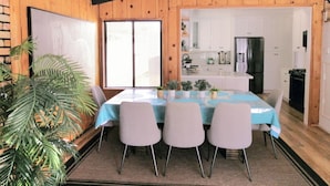A dining area with a table set for four, surrounded by chairs, in a room with wooden walls and a kitchen visible through an open door. - Bright beach-city home — newly renovated. Only 3 mi. from SoCal beaches!   (Torrance)