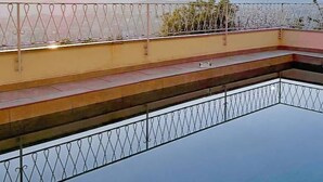Piscina no terraço com grade de metal e vista para montanhas distantes ao pôr do sol.