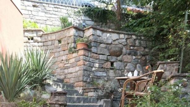 Uma escadaria de pedra com design rústico, cercada por vegetação e uma cadeira de vime.