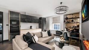A modern living room with a sofa, ottoman, and a dining area with a chandelier. - Near Transport - Hot tub - Fireplace - Sleeps 2 (Edinburgh)