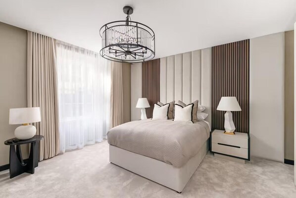 Een moderne hotelkamer met een groot bed, twee nachtkastjes met lampen, een kroonluchter en een groot raam met gordijnen.