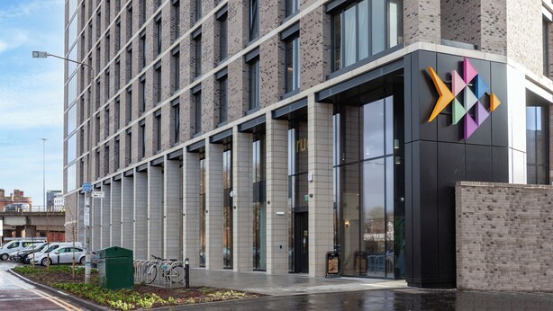 A modern building with a glass facade and a distinctive colorful logo on the right side. - Student Only True Glasgow (Glasgow)