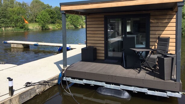 A floating house with a deck, outdoor seating, and a view of the water. - Hausboot KHT 2 Lacet mit Elektrokamin im Salon, 1 Schlafraum, Küche, Duschbad m by Interhome (Wilhelmshaven)